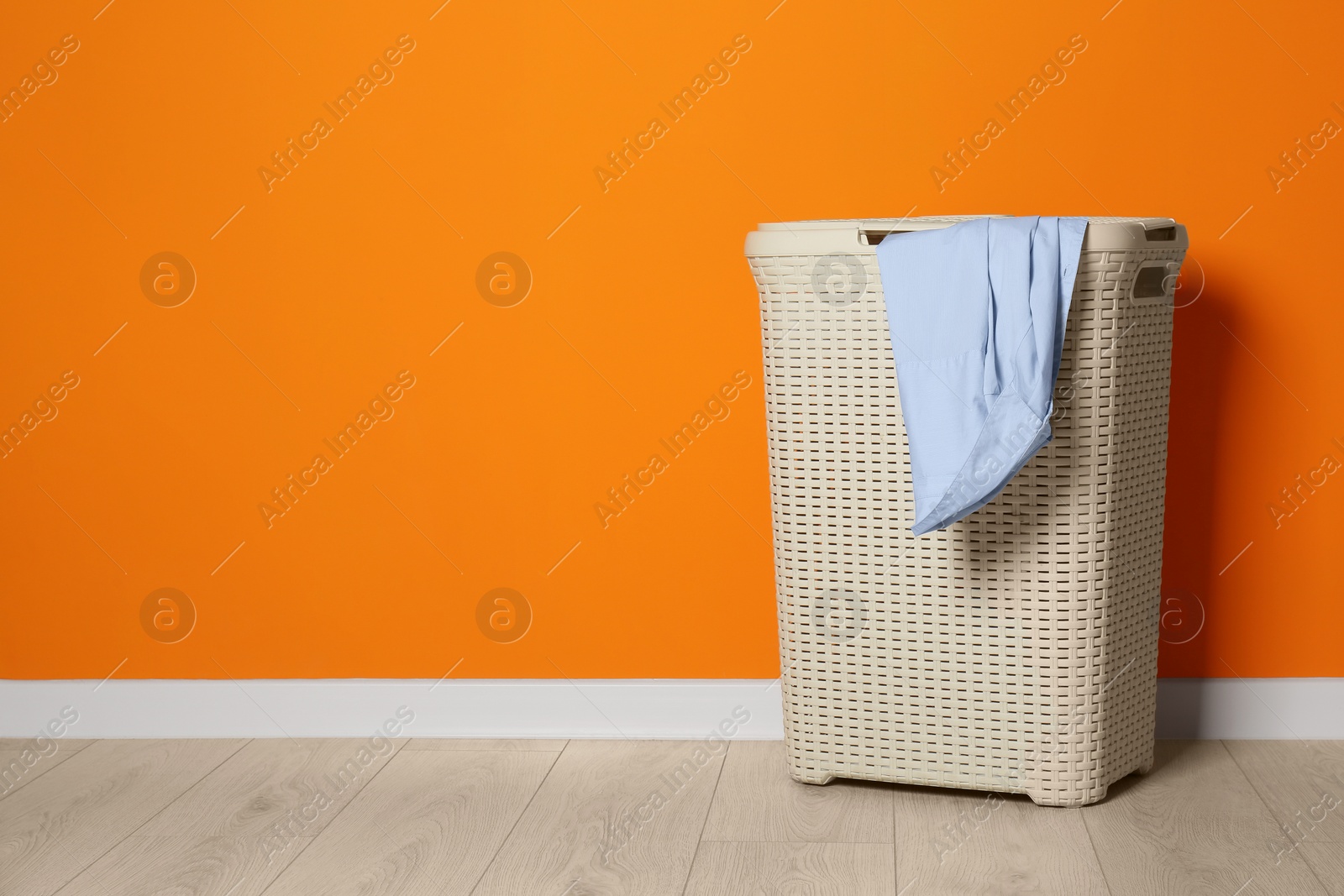 Photo of Laundry basket near orange wall indoors, space for text