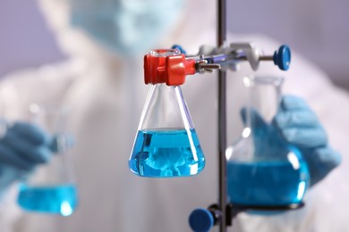 Scientist holding flasks with light blue liquid on grey background, closeup