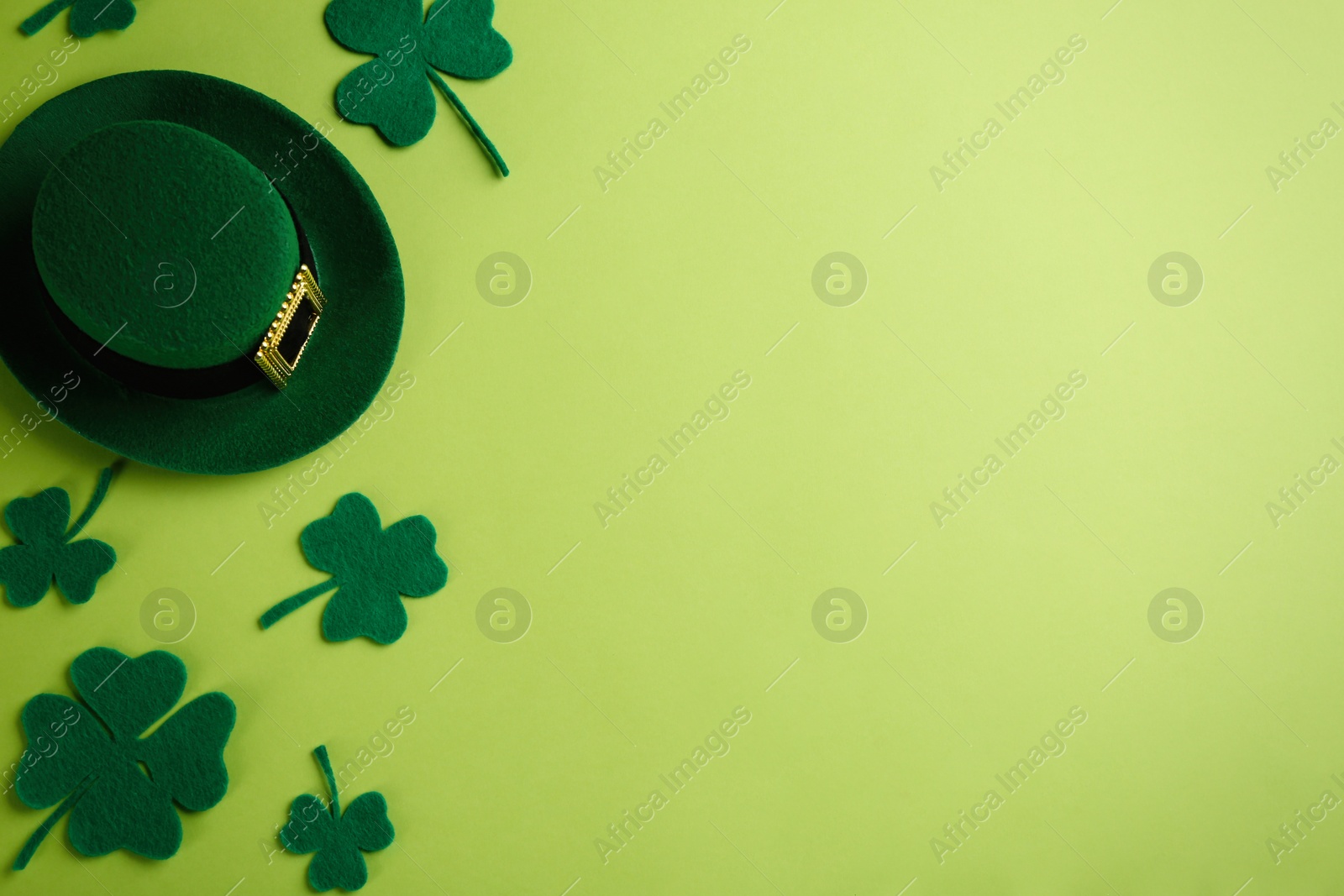 Photo of Leprechaun's hat and decorative clover leaves on green background, flat lay with space for text. St. Patrick's day celebration