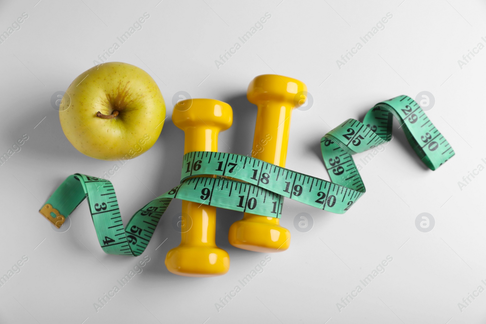 Photo of Measuring tape, dumbbells and apple on white background, flat lay. Weight control concept