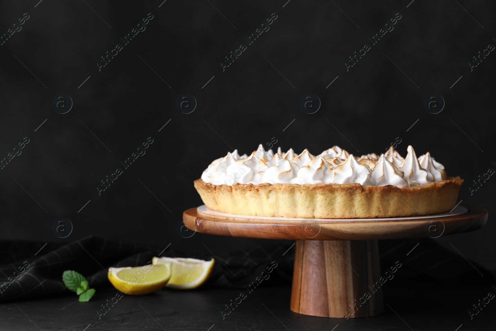 Photo of Stand with delicious lemon meringue pie on table against black background