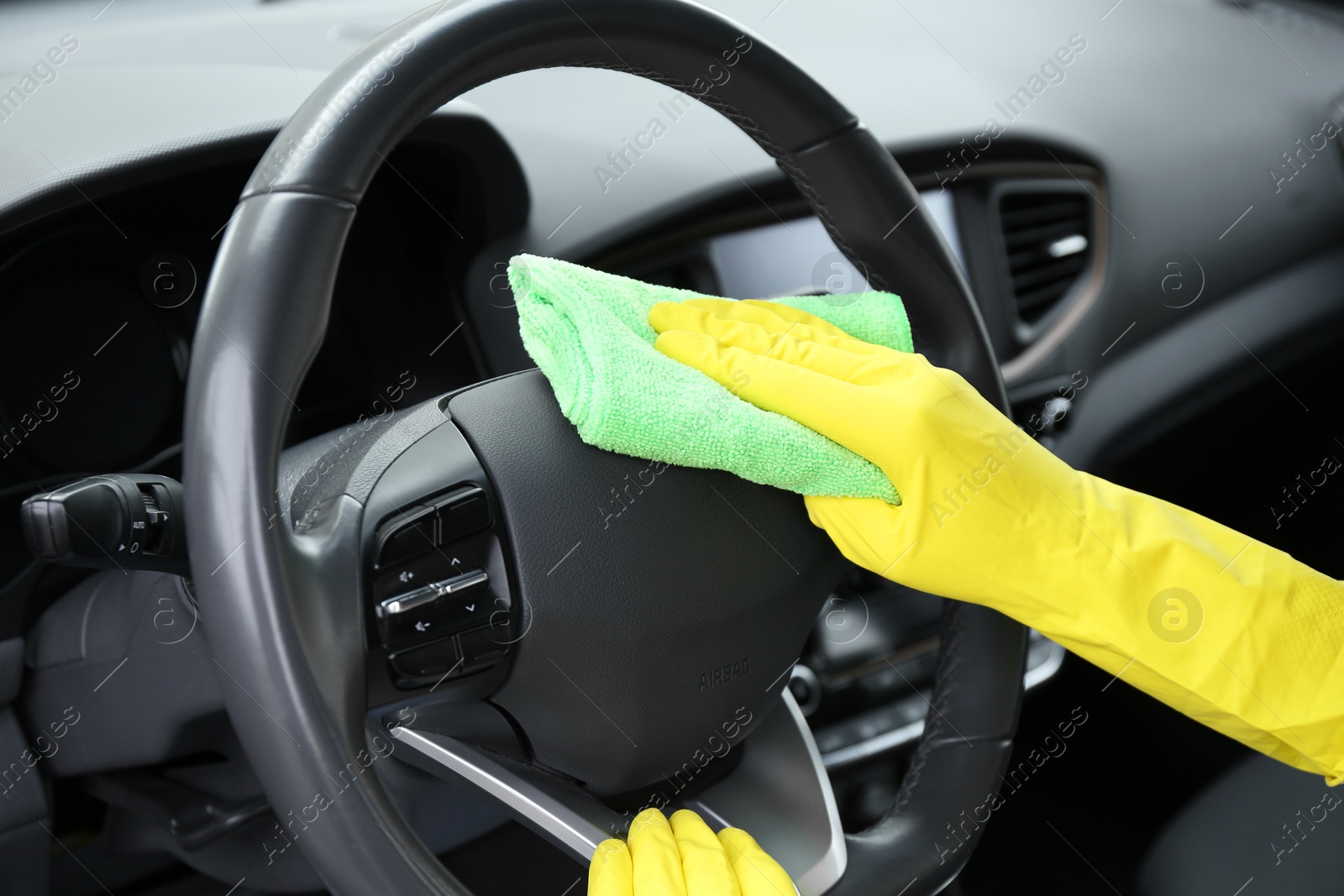 Photo of Woman cleaning steering wheel with rag in car, closeup