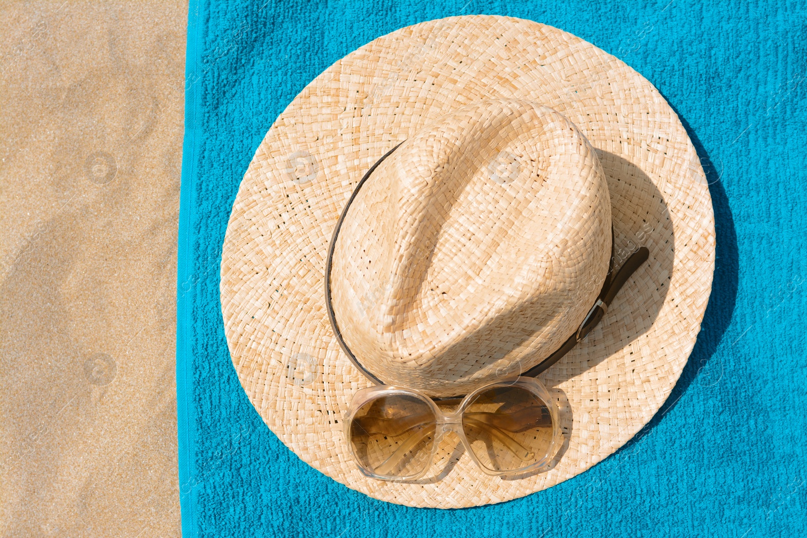 Photo of Soft blue beach towel with straw hat and sunglasses on sand, flat lay