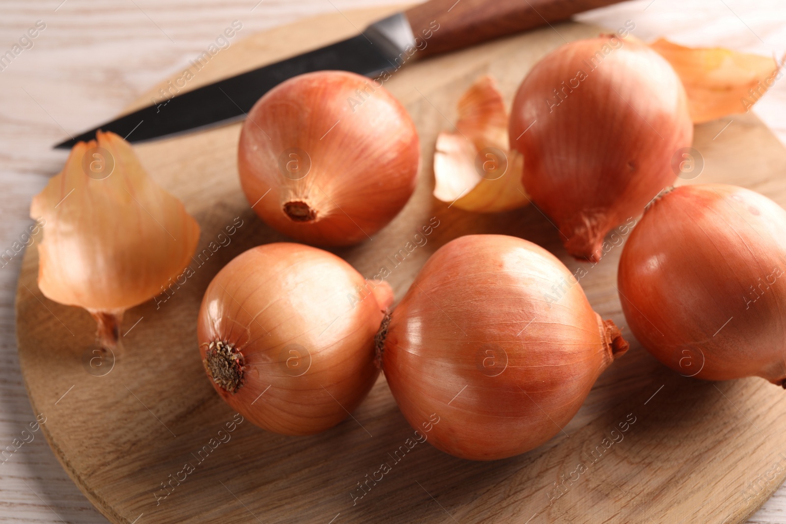 Photo of Tray with ripe onions and knife on wooden table, closeup