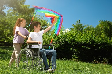 Happy teenage boy in wheelchair with kite and girl at park on sunny day
