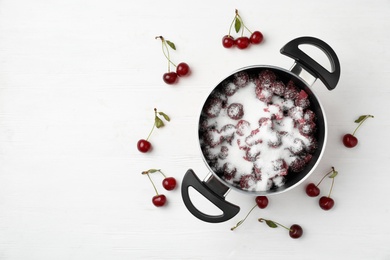 Photo of Pot with cherries and sugar on white wooden table, space for text. Making delicious jam