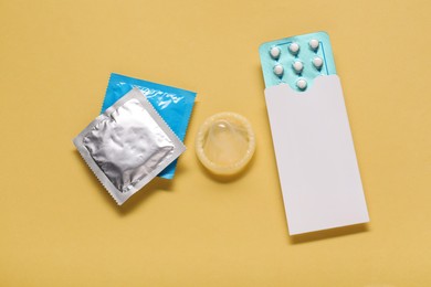 Photo of Condoms and birth control pills on yellow background, flat lay. Choosing method of contraception