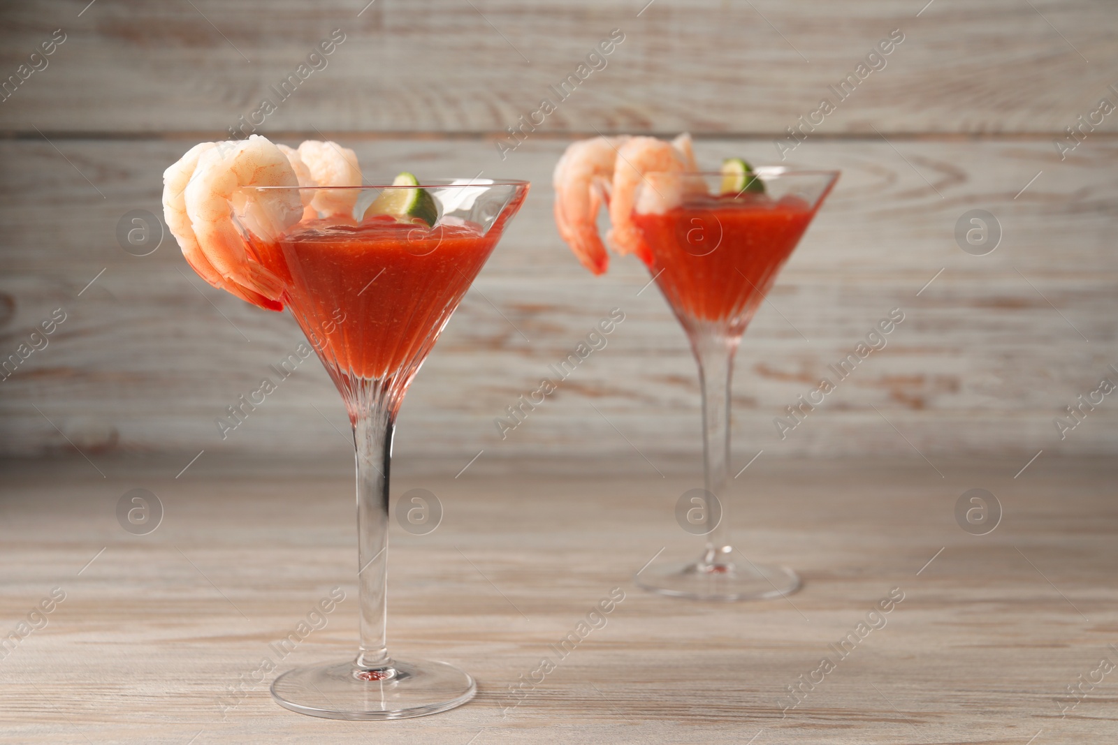 Photo of Tasty shrimp cocktail with sauce and lime in glasses on wooden table