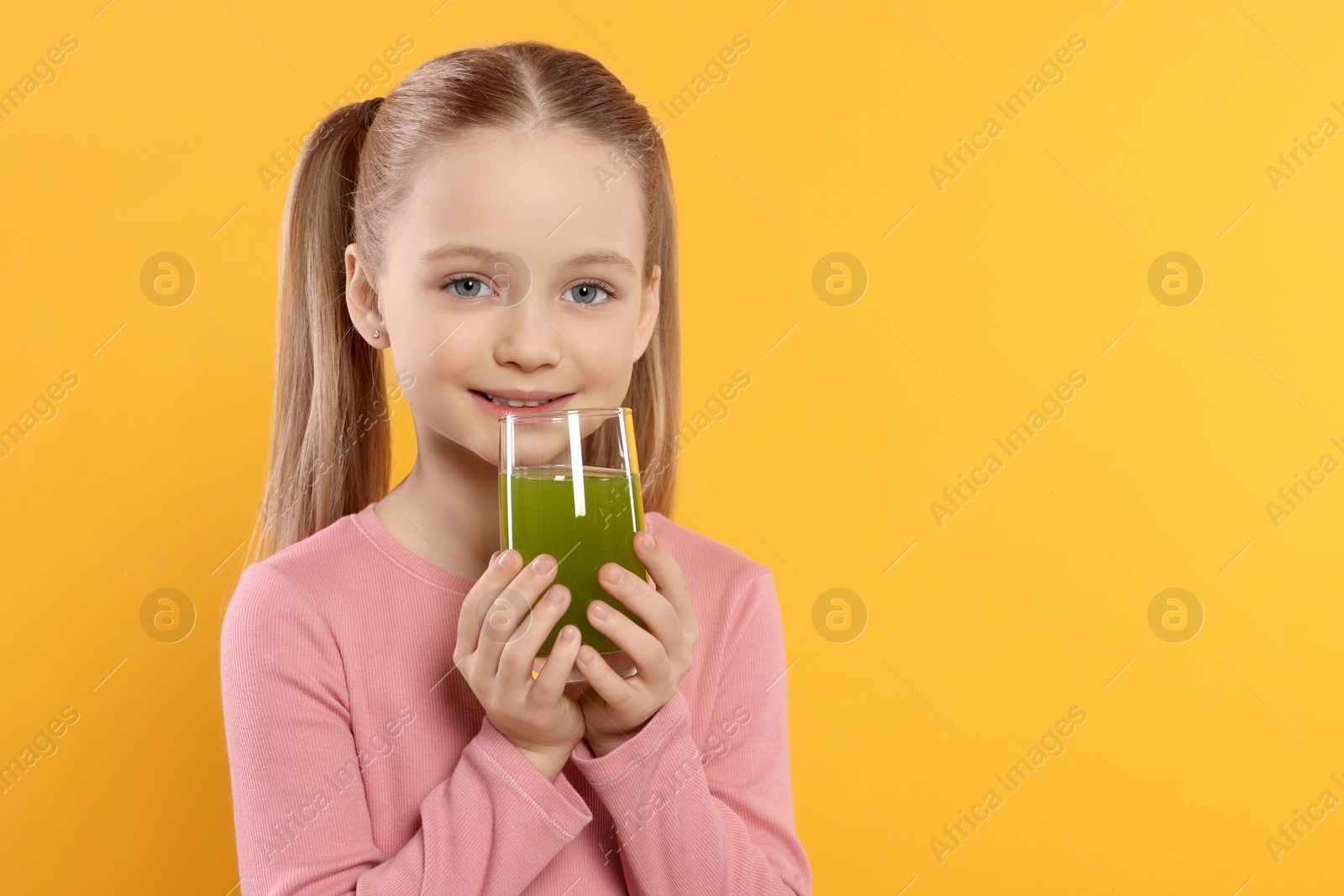Photo of Cute little girl with glass of fresh juice on orange background, space for text
