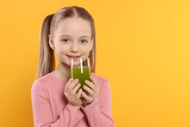 Cute little girl with glass of fresh juice on orange background, space for text