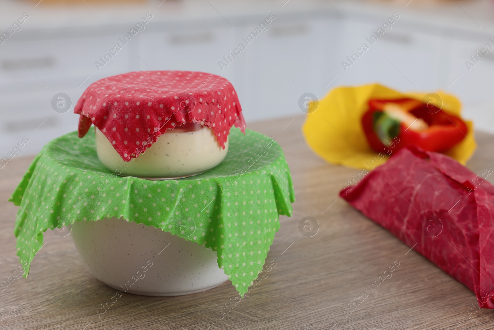 Photo of Bowls covered with beeswax food wraps on wooden table in kitchen