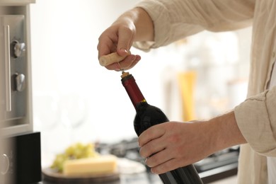 Photo of Man opening wine bottle with corkscrew indoors, closeup