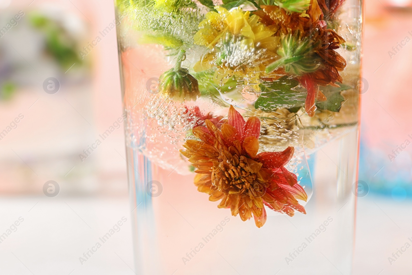 Photo of Glass of ice cubes with flowers on blurred background, closeup