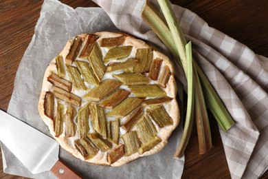 Photo of Freshly baked rhubarb pie, stalks and spatula on wooden table, flat lay