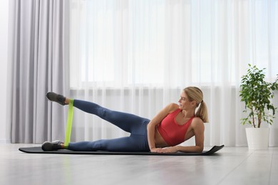 Athletic woman doing exercise with fitness elastic band on mat at home