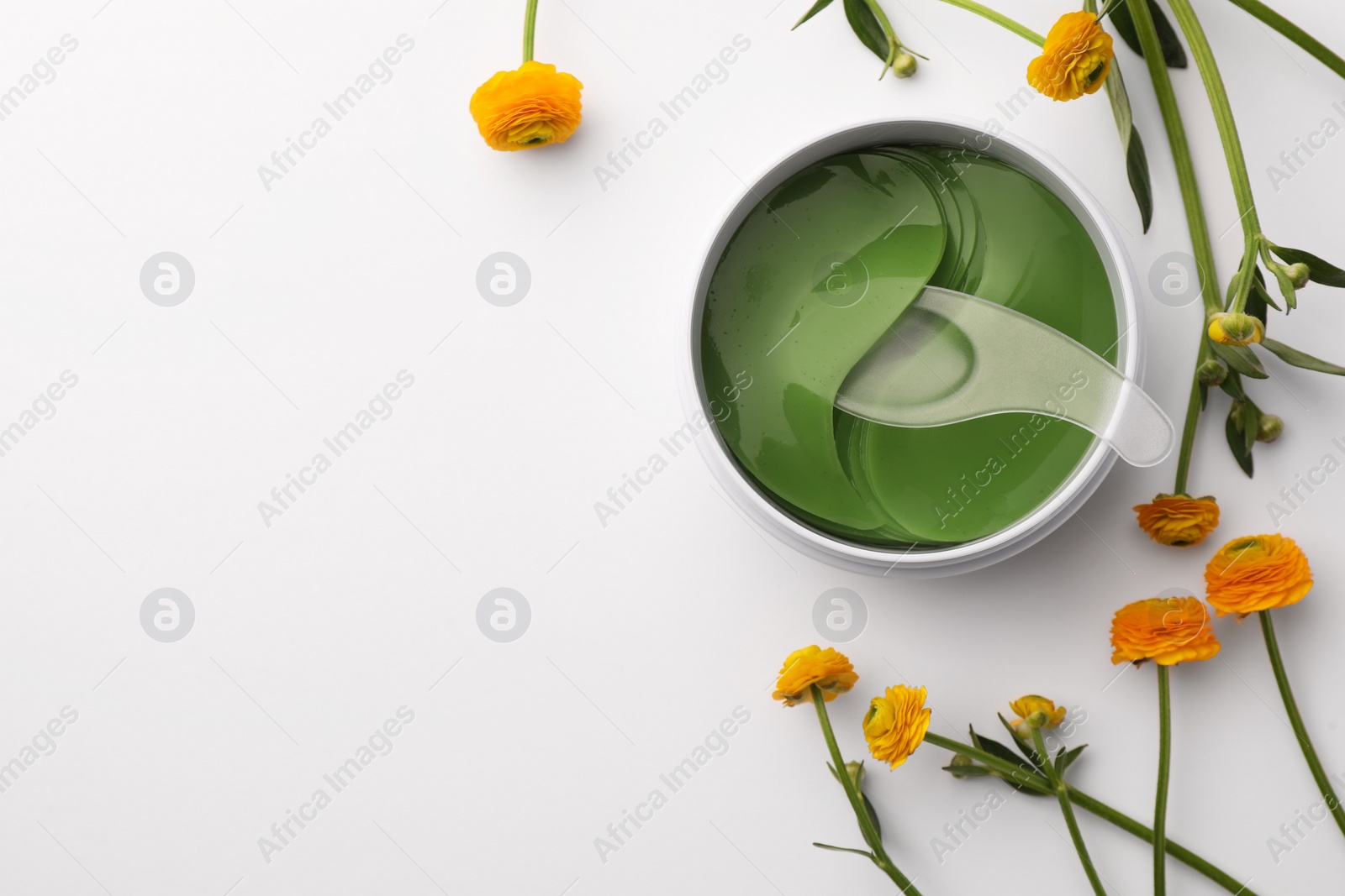 Photo of Jar of under eye patches with spoon and flowers on white background, flat lay with space for text. Cosmetic product