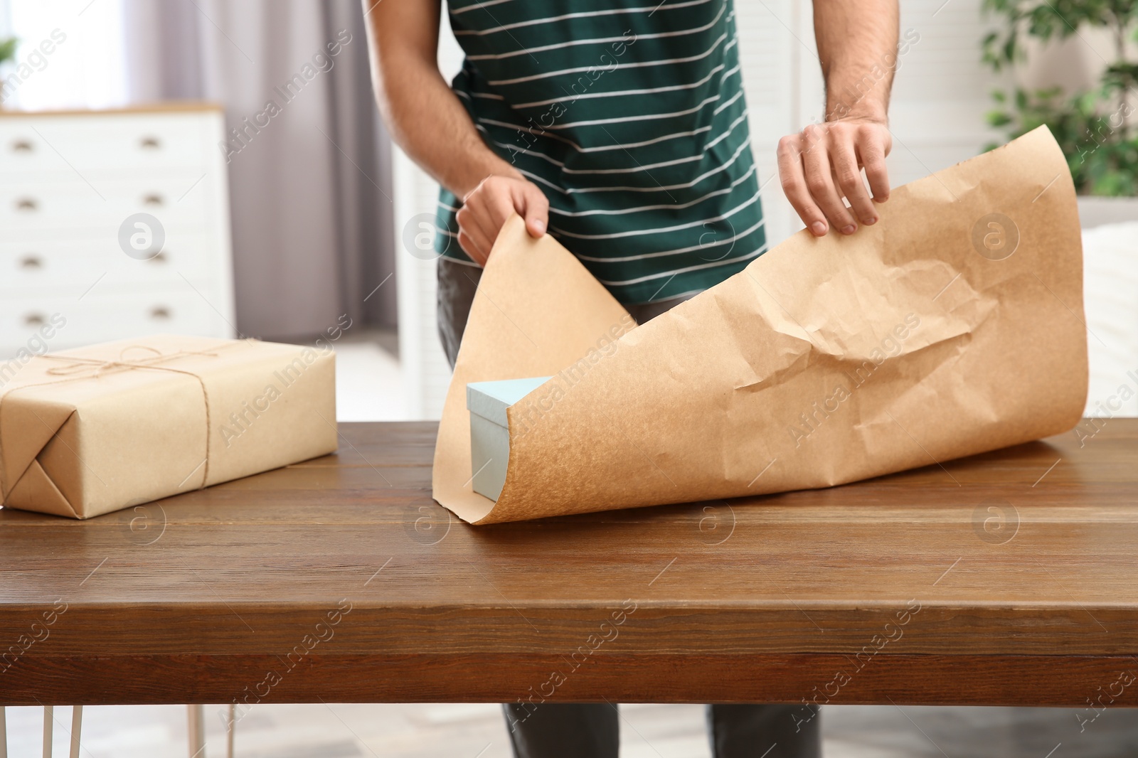 Photo of Young man wrapping parcel on table at home, closeup