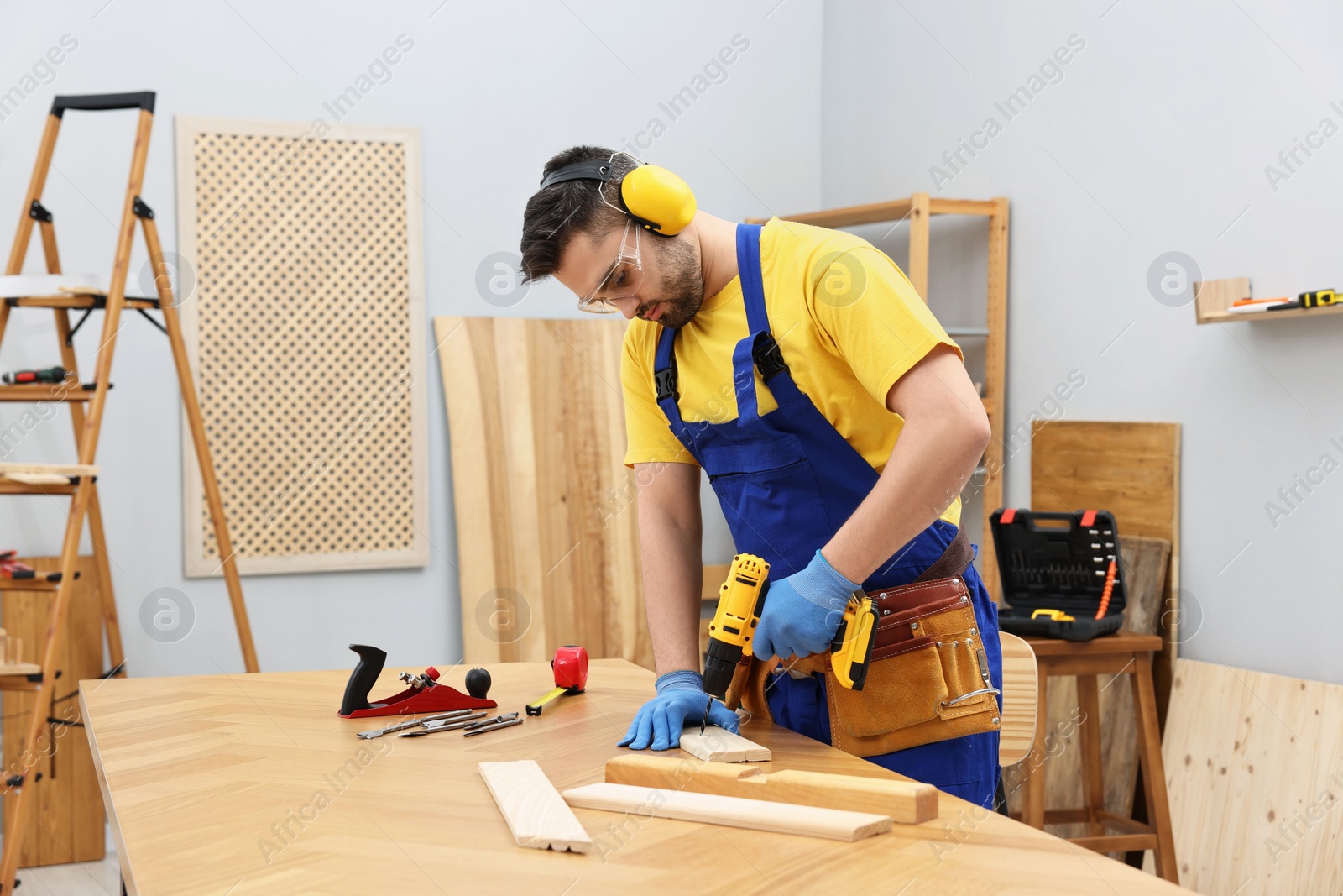 Photo of Young worker using electric drill at table in workshop