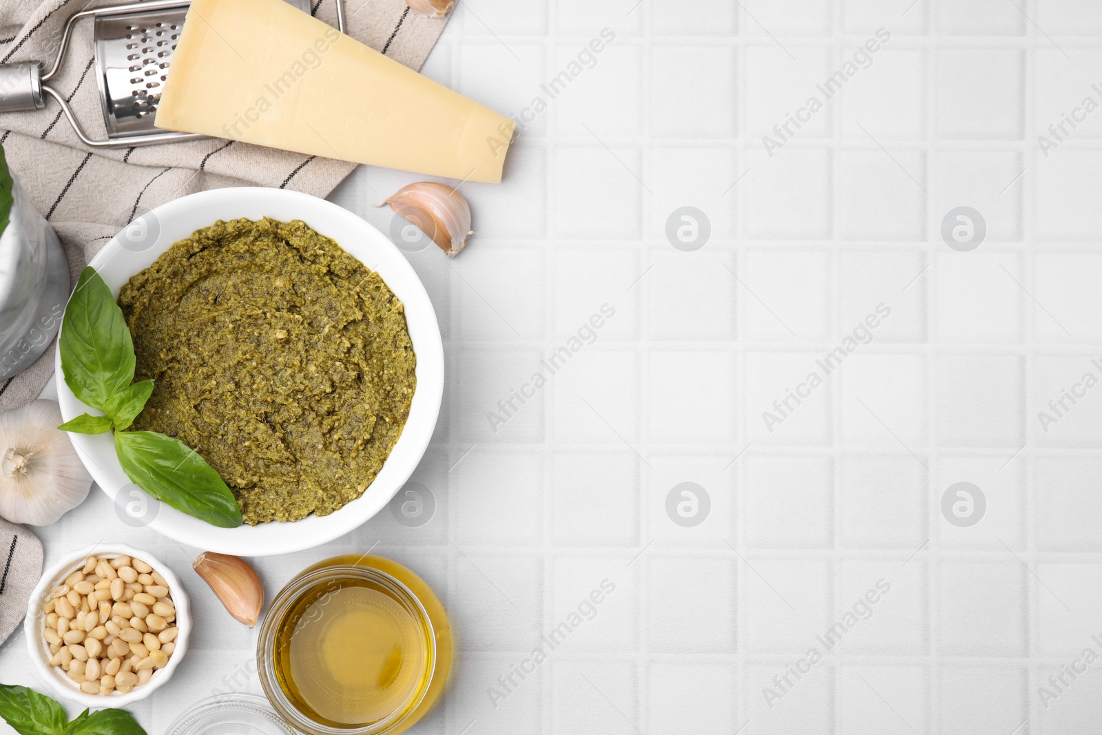 Photo of Tasty pesto sauce and ingredients on white tiled table, flat lay. Space for text