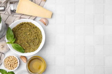Photo of Tasty pesto sauce and ingredients on white tiled table, flat lay. Space for text