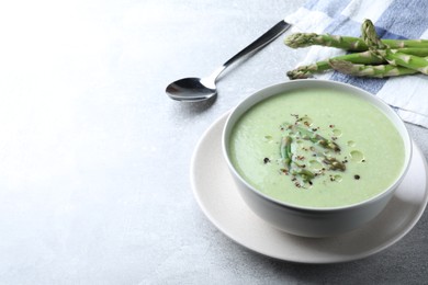 Photo of Delicious asparagus soup served on light grey table, space for text