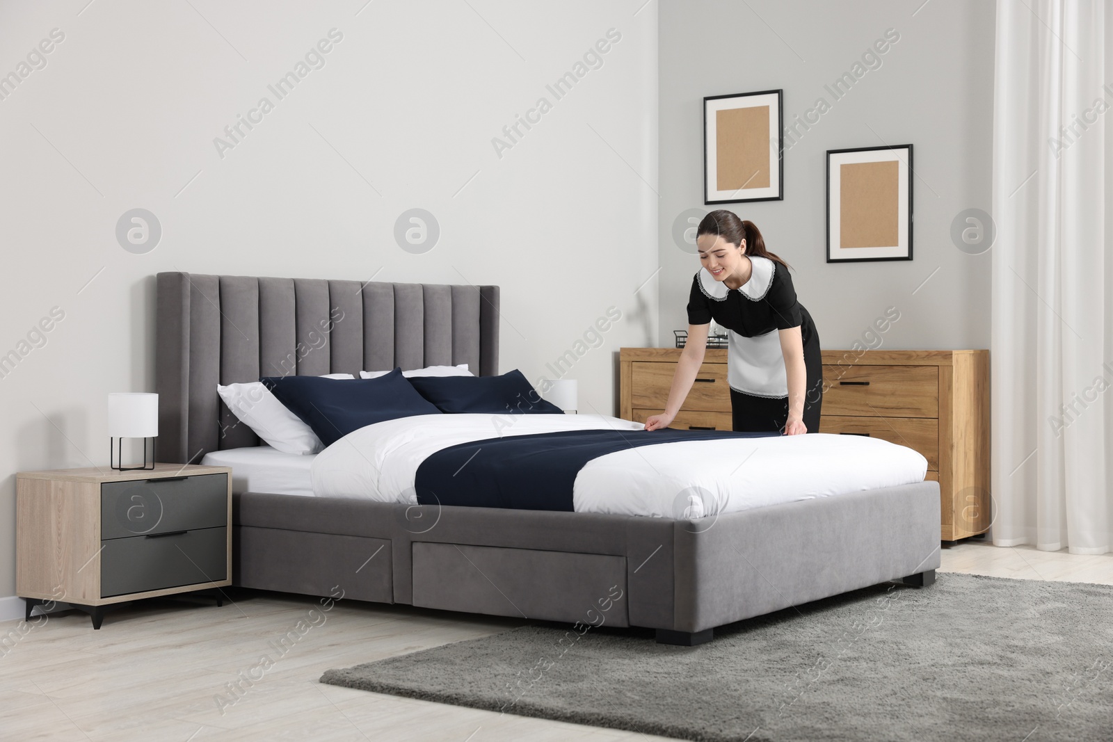 Photo of Young chambermaid making bed in hotel room