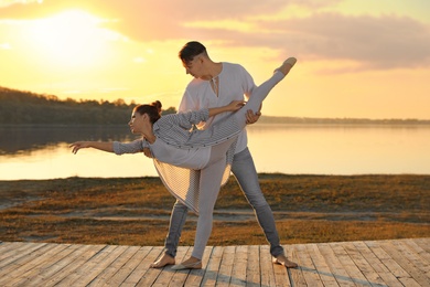 Beautiful young couple practicing dance moves near river at sunset