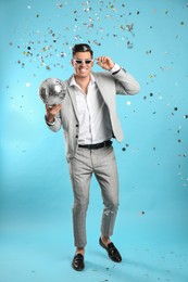 Happy man with disco ball and confetti on light blue background