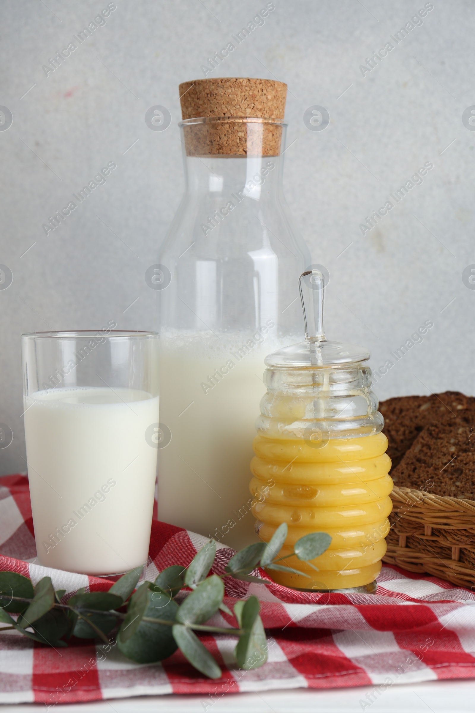 Photo of Jar with tasty honey, milk and bread on checkered cloth