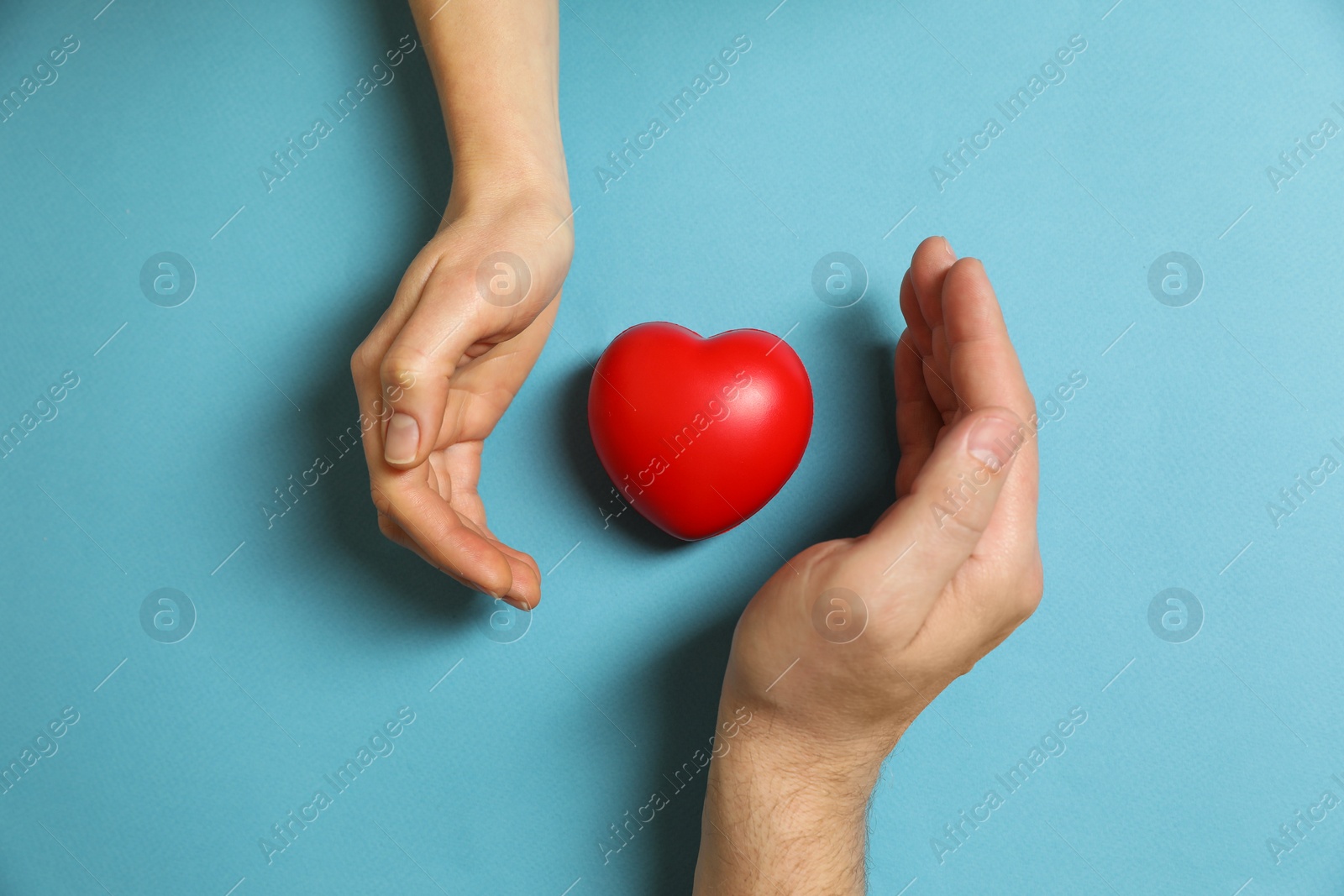 Photo of Couple protecting red decorative heart on light blue background, top view