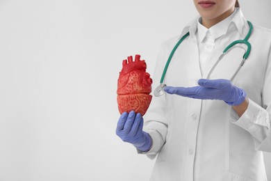 Photo of Closeup view of doctor with stethoscope and model of heart on white background, space for text. Cardiology concept