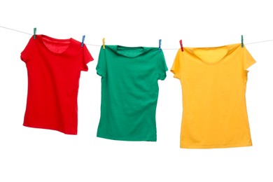 Photo of Different bright t-shirts drying on washing line against white background