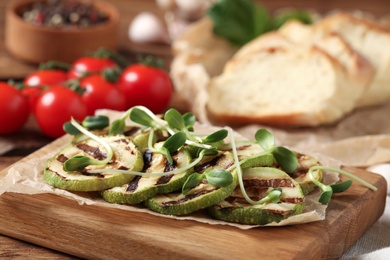 Photo of Delicious grilled zucchini slices with microgreens on wooden board, closeup