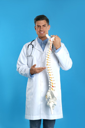 Photo of Male orthopedist with human spine model against blue background
