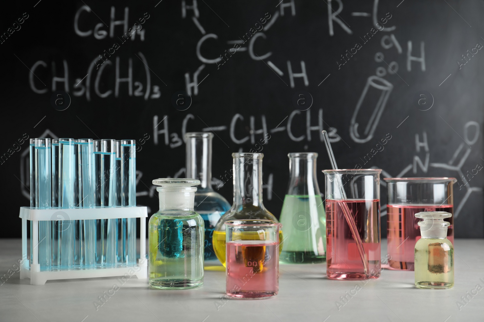 Photo of Laboratory glassware on table against blackboard with chemical formulas