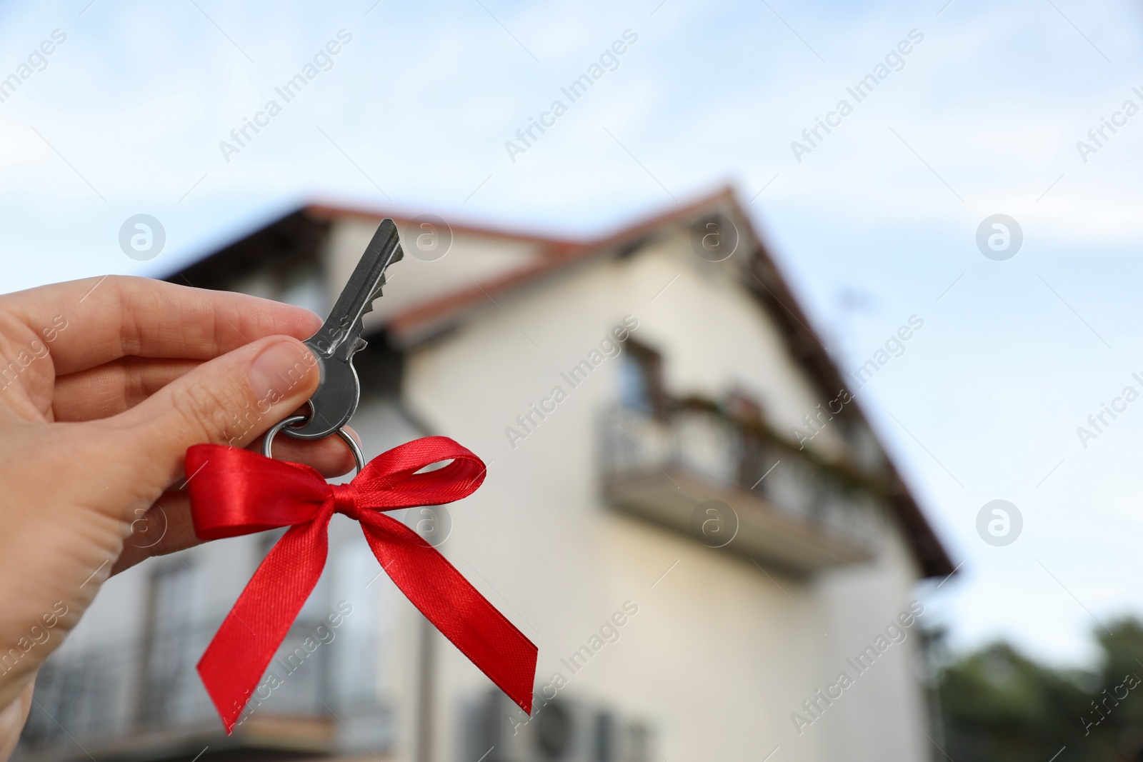 Photo of Woman holding key with bow near house outdoors, closeup. Space for text