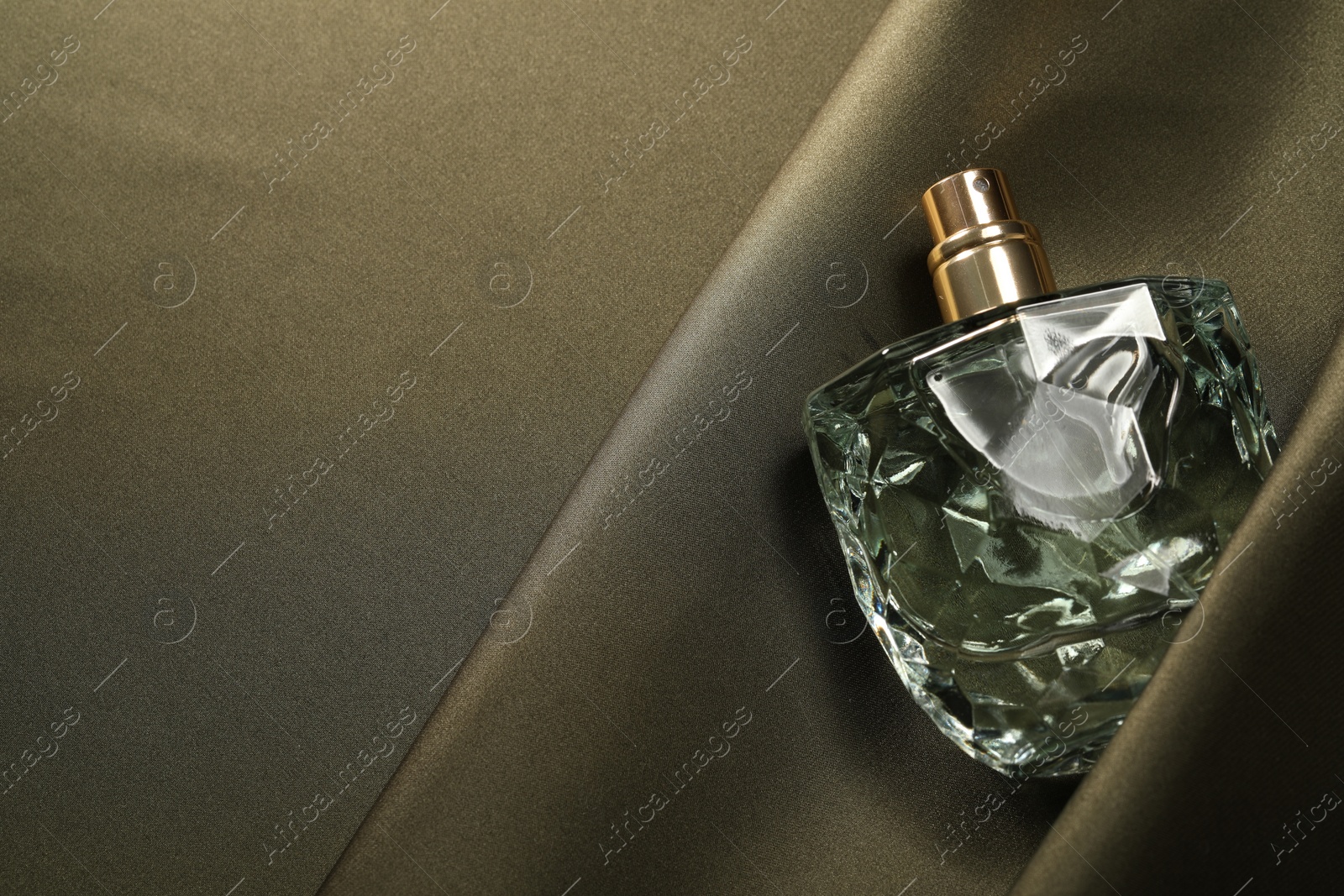 Photo of Luxury perfume in bottle on dark silk fabric, top view