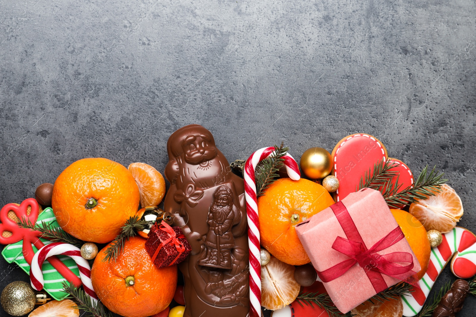 Photo of Flat lay composition with chocolate Santa Claus candies on grey table. Space for text