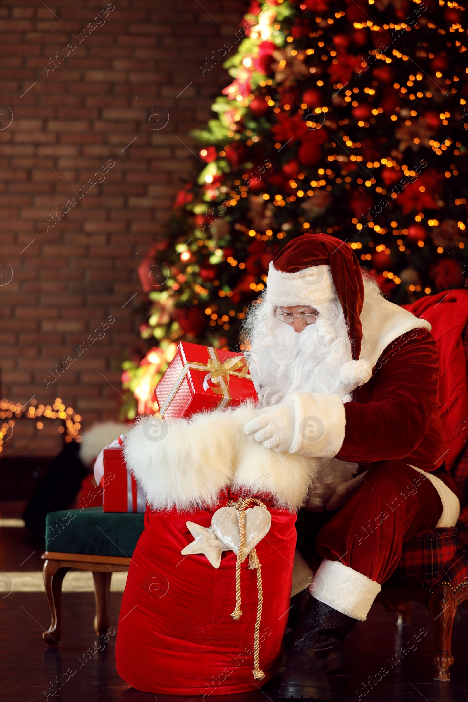 Photo of Santa Claus with gift sack near Christmas tree indoors