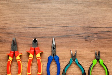 Photo of Different pliers on wooden table, flat lay. Space for text