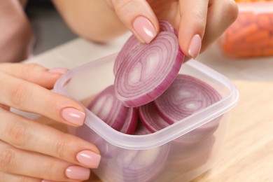 Photo of Woman putting cut onion into plastic container at table, closeup. Food storage