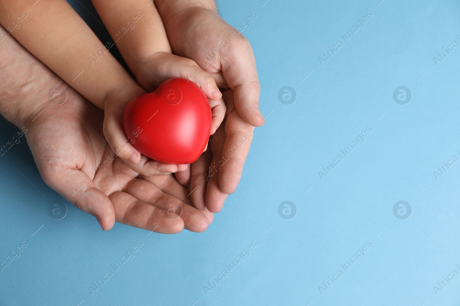 Photo of Father and his child holding red decorative heart on light blue background, top view. Space for text