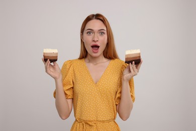 Photo of Emotional young woman with pieces of tasty cake on light grey background