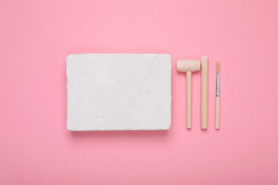 Photo of Educational toy for motor skills development. Excavation kit (plaster, digging tools and brush) on pink background, flat lay