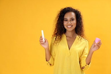 Young African American woman with tampon and menstrual cup on yellow background