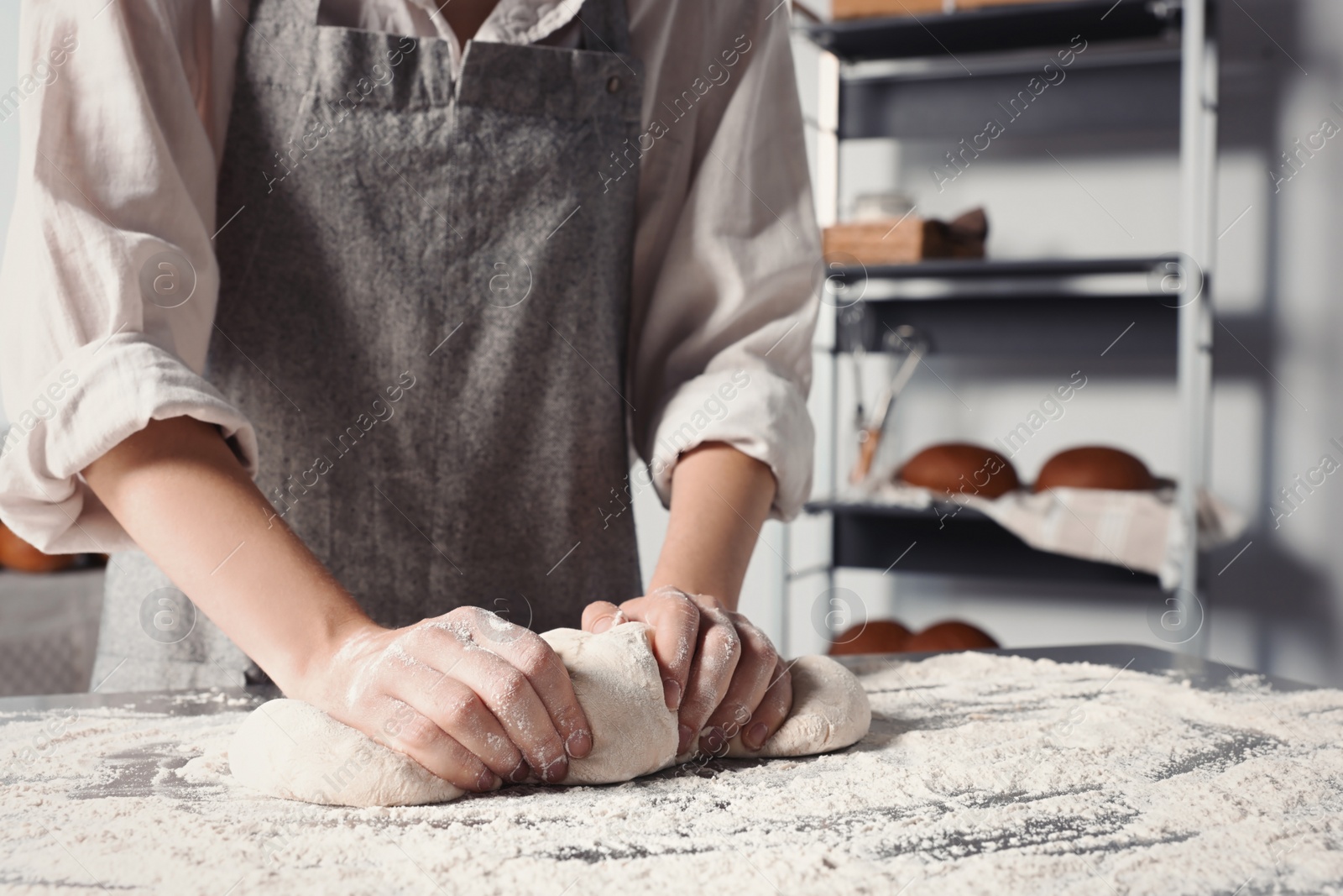 Photo of Woman kneading dough at table in kitchen, closeup