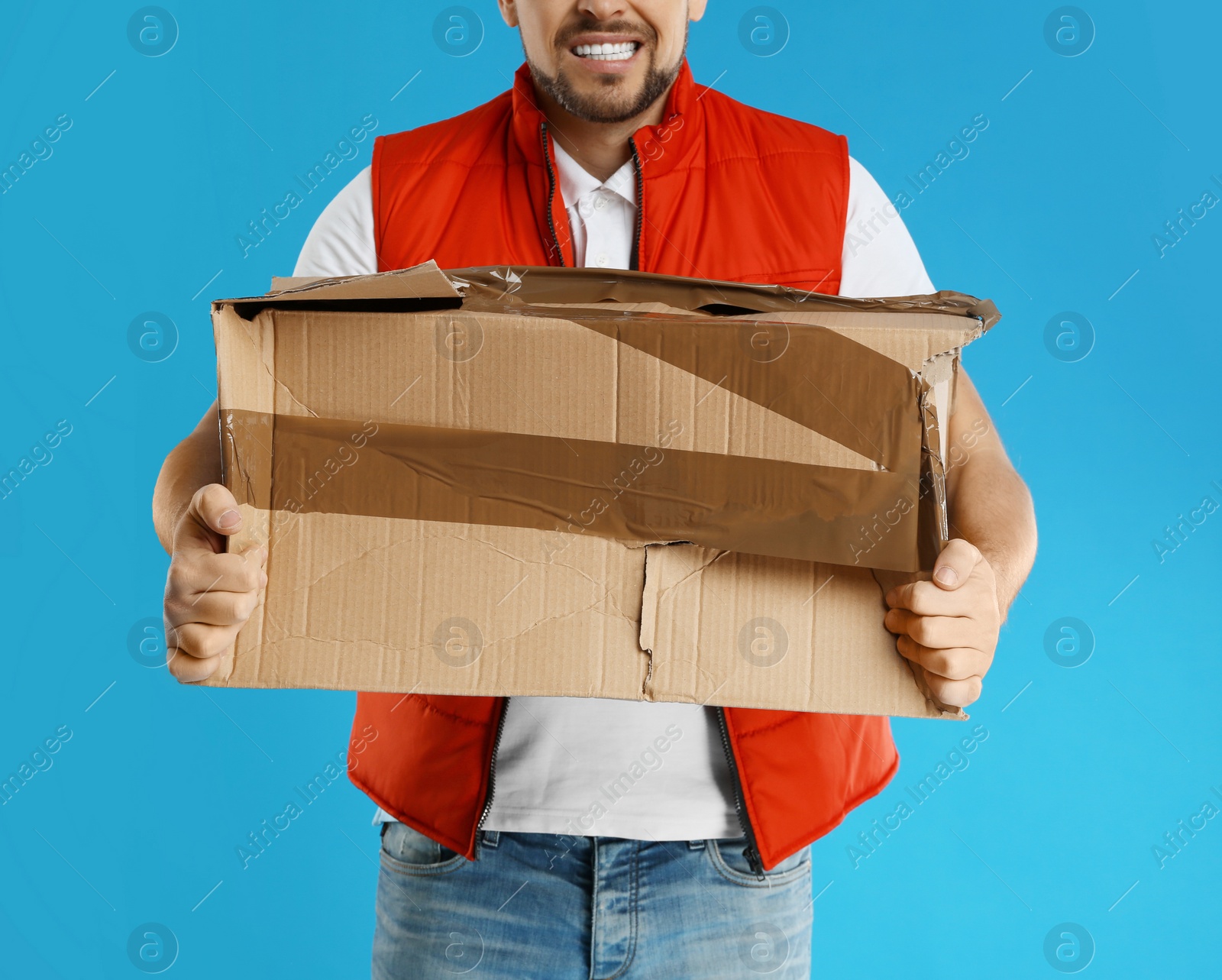 Photo of Emotional courier with damaged cardboard box on blue background, closeup. Poor quality delivery service