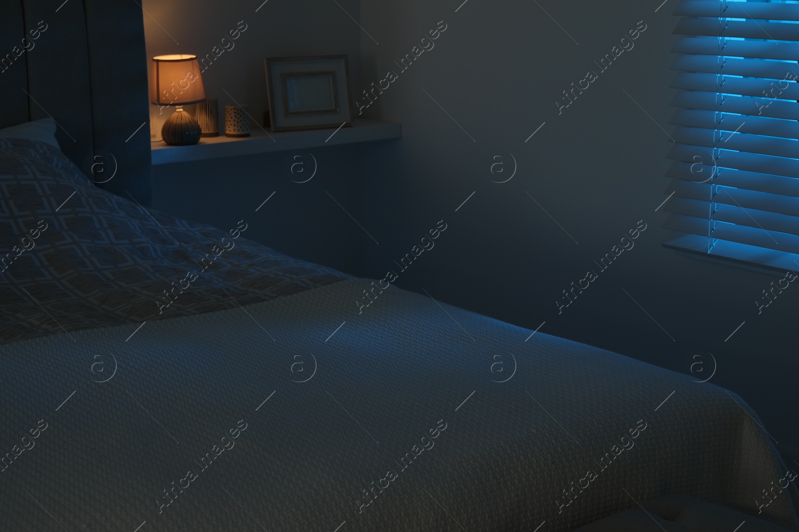 Photo of Large bed and shelf with accessories in stylish bedroom at night
