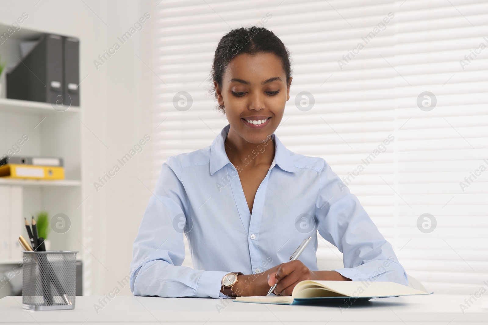 Photo of Smiling African American intern working at white table in office