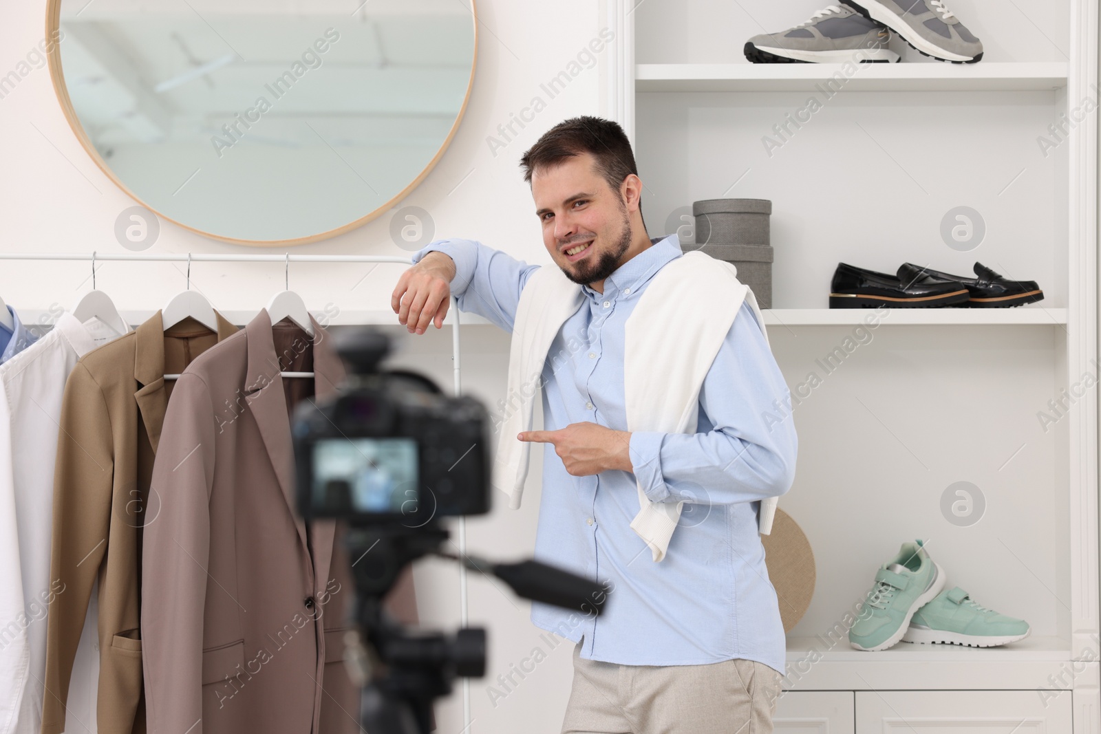 Photo of Smiling fashion blogger showing clothes while recording video at home